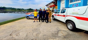 Radiowóz straży pożarnej, policjanci, strażacy oraz ratownicy wodni na tle zalewu.