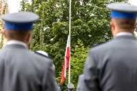 Dwóch policjantów stojących tyłem pomiędzy nimi widać flagę państwową.