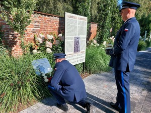 Komendant składa kwiaty pod tablicą pamiątkowa, policjant stoi.