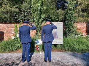 Komendant oraz policjant stoją tyłem i salutują przed tablicą pamiątkową.