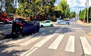 Samochód leżący na boku, auto na skrzyżowaniu, radiowóz policyjny oraz wóz strażacki.