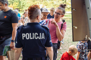 Napis policja na koszulce policjantki i rozmawiająca kobieta z dzieckiem.