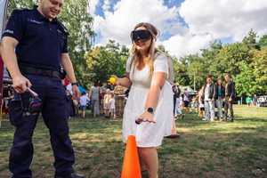 Policjant i kobieta w alkogoglach idąca pomiędzy pachołkami.