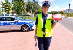 Policjantka trzymającą w dłoni apteczkę obok radiowóz.