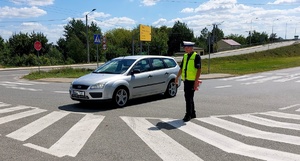 Policjant idący z apteczką i zatrzymujący samochód.