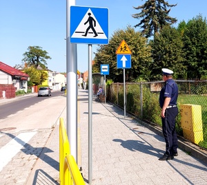 Policjant w mundurze stojący przy znakach drogowych obok szkoły.