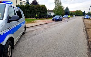 Radiowozy policyjne i auto na poboczu. Policjanci w mundurach podczas czynności na wypadku.