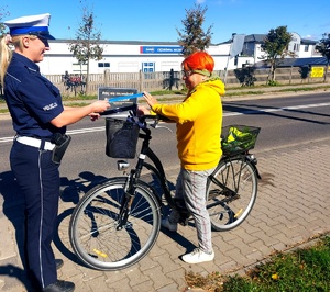 Policjantka wręczająca opaskę odblaskową rowerzystce.