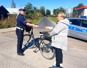 Policjantka wręczająca odblask rowerzystce obok radiowóz.