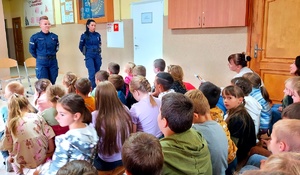Policjantki stojące przed dziećmi siedzącymi w ławkach.