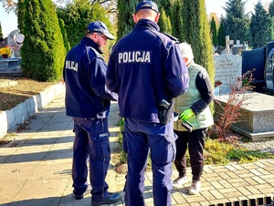 Policjanci rozmawiający z kobieta na cmentarzu.