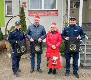 Dwoje policjantów oraz burmistrz i pani sołtys wszyscy z workami z prezentami dla dzieci przed budynkiem urzędu miasta.