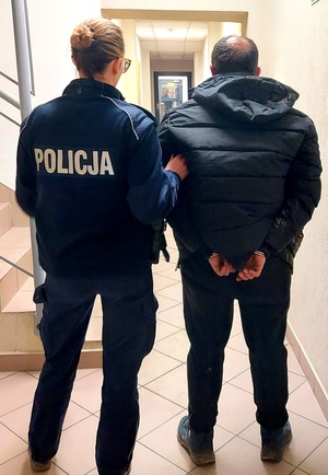 Policjantka trzymająca zatrzymanego w kajdankach.