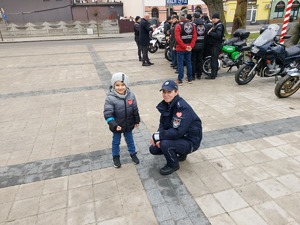 Policjantka kucająca obok małego chłopca, który na rękawie kurtki ma odblask.