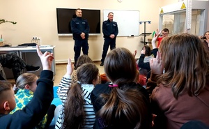 Policjanci stojący przed dziećmi siedzącymi w sali.