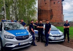 Policjanci przy radiowozie na tle ruin zamku.
