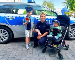 Policjantka kucająca obok dzieci przy radiowozie.