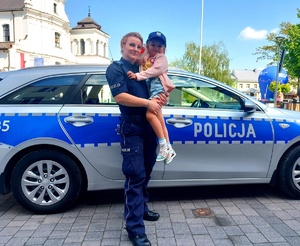 Policjantka trzymająca na rękach dziewczynkę obok radiowozu.