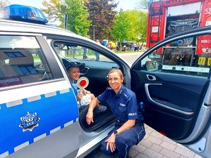 Policjantka kucająca obok chłopca przy radiowozie.