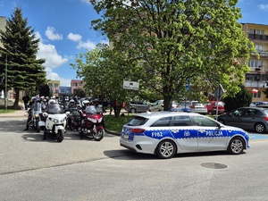 Radiowóz policyjny oraz motocykliści za nim stojący na drodze.