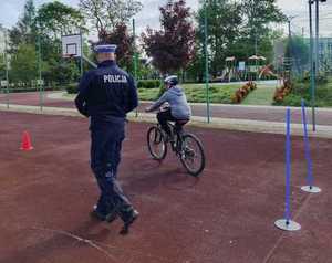 Policjant idący obok dziecka jadącego na rowerze.