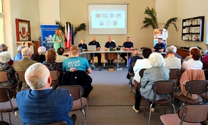 Policjanci siedzący przy stole przed nimi seniorzy.