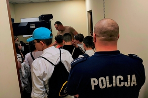 Policjant stojący tyłem i dzieci w pokoju technika kryminalistyki.