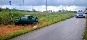 Samochód z pogiętą karoserią w trawie oraz radiowóz na drodze.