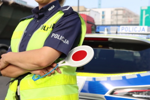 Policjant z tarczą w ręce oraz radiowóz.