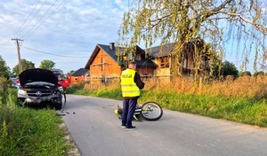 Policjant w kamizelce odblaskowej przy motocyklu i w oddali rozbity samochów.