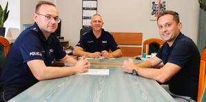 Dwóch policjantów oraz mężczyzna siedzący przy stole.