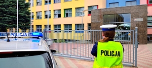 Policjantka stojąca obok radiowozu przy szkole.