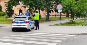 Policjant obok radiowozu przy szkole.
