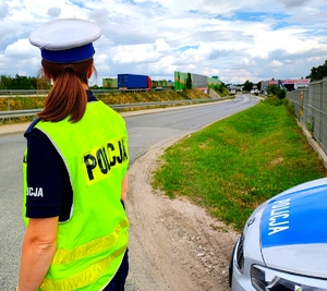 Policjantka stojąca przy drodze i radiowóz.