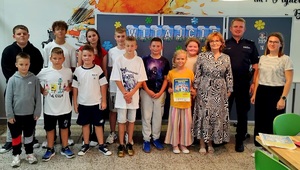 Policjant, dzieci i nauczyciele promują konkurs.