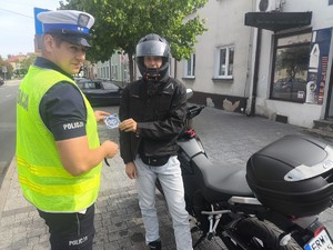 Umundurowany policjant ruchu drogowego wręczający motocykliście naklejkę profilaktyczną.