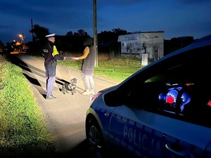Policjant wręczający odblask pieszej z psem, część radiowozu.