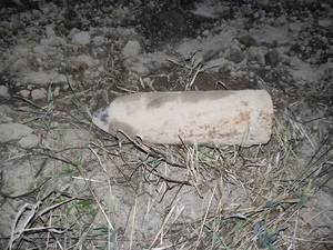 Pocisk artyleryjski leżący na trawie obok pole orne.