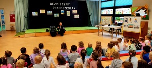 Policjantka kucająca przy foteliku samochodowym, przed nią dzieci siedzące na podłodze w sali.