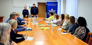 Komendant, policjantka stoją przed nauczycielami, którzy siedzą w sali konferencyjnej komendy.
