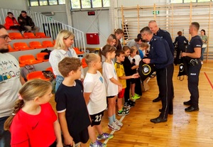 Policjanci wręczają nagrody dzieciom i gratulują.