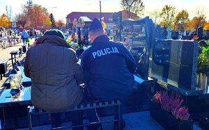 Policjant siedzący ze starszą kobieta na ławce przy grobie.