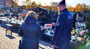 Policjant dający ulotkę kobiecie na cmentarzu.
