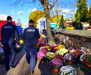 Policjanci idący chodnikiem wzdłuż kwiaty.