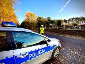 Policjantka stojącą przy radiowozie w tle cmentarz.