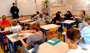 Policjantka rozmawiająca z dziećmi siedzącymi w ławkach szkolnych.
