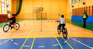 Policjant w kamizelce i dwoje dzieci jadących na rowerze po torze przeszkód.