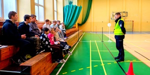 Policjant rozmawiający dziećmi siedzącymi na ławkach przed egzaminem.