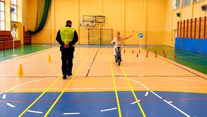 Policjant idący obok dziecka jadącego na rowerze.