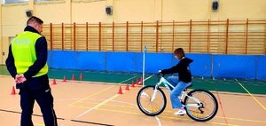 Policjant w kamizelce i dziewczynka jadąca na rowerze.